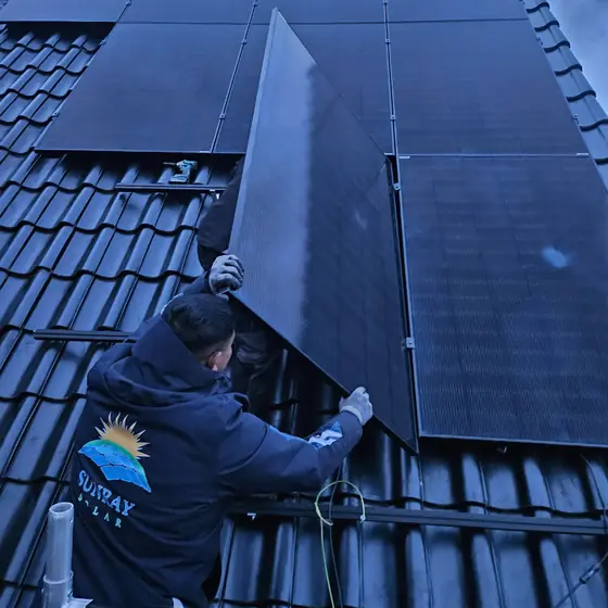 Installateur in een Sunray Solar-jas werkt aan een zonnepaneel op een dak