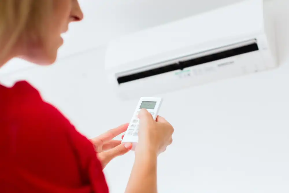 Vrouw bedient een airco aan de muur met een afstandsbediening